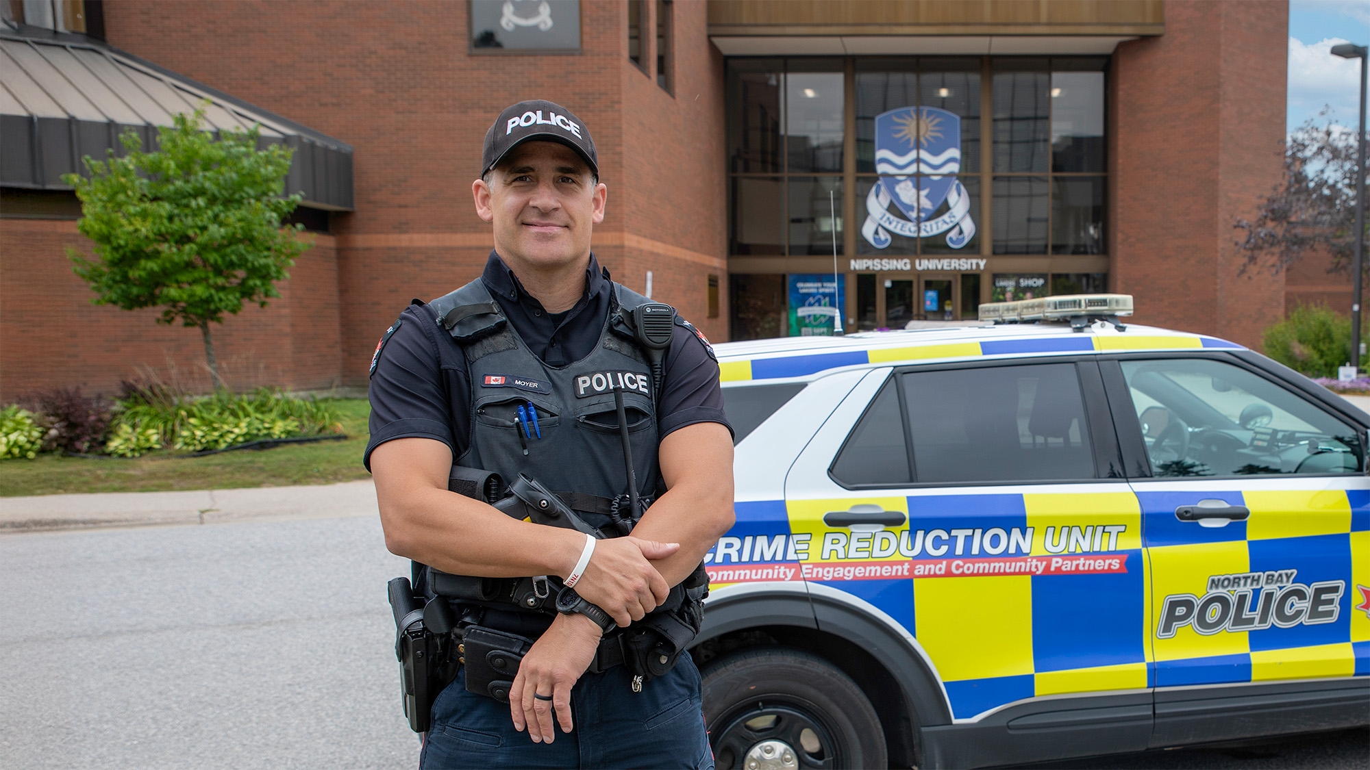 A police office with his police vehicle in front of Nipissing front extrance