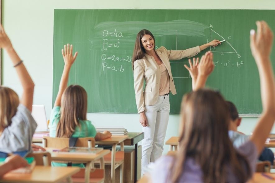 a teacher writing on a chalk board while students raise their hands