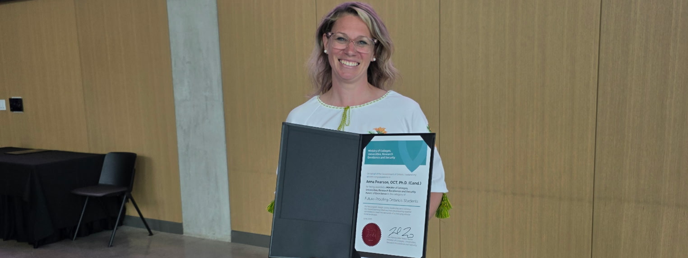 Anna Pearson stands smiling whilst holding her Minister's Award of Excellence