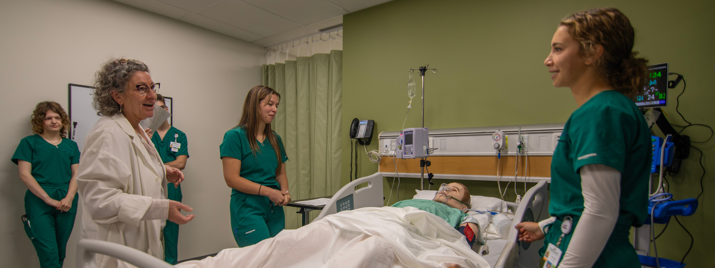 Nursing students and an instructor stand beside a simulation centre patient bed.