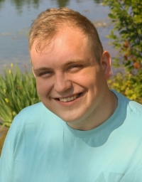 A man in light blue t-shirt against a water background