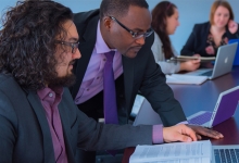 School of Business associates sit around a board table analyzing data on computers.