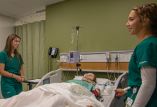 Nursing students and an instructor stand beside a simulation centre patient bed.