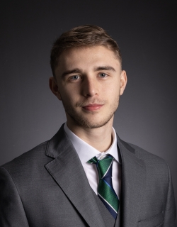 Hayden Lloyd smiles at the camera dressed in a grey suit. 
