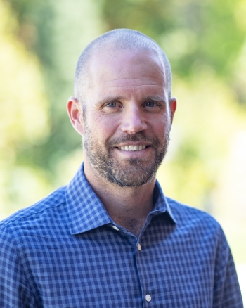 Dr. Graydon Raymer smiling with a blurred forest background behind him. 